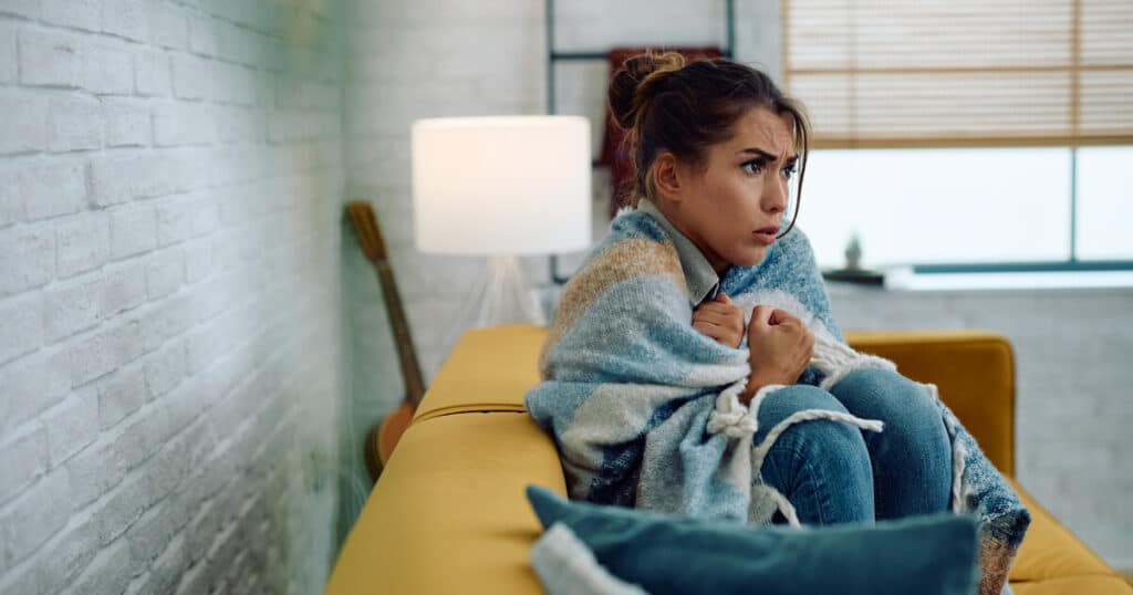 Woman wrapped in blanket looking cold in a room, HVAC troubleshooting tips from SwiftPro.