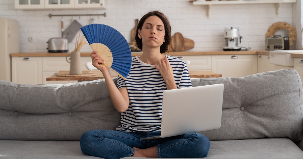AC fan not spinning? A woman is fanning herself in the summer heat because her air conditioner fan is not working as it should.