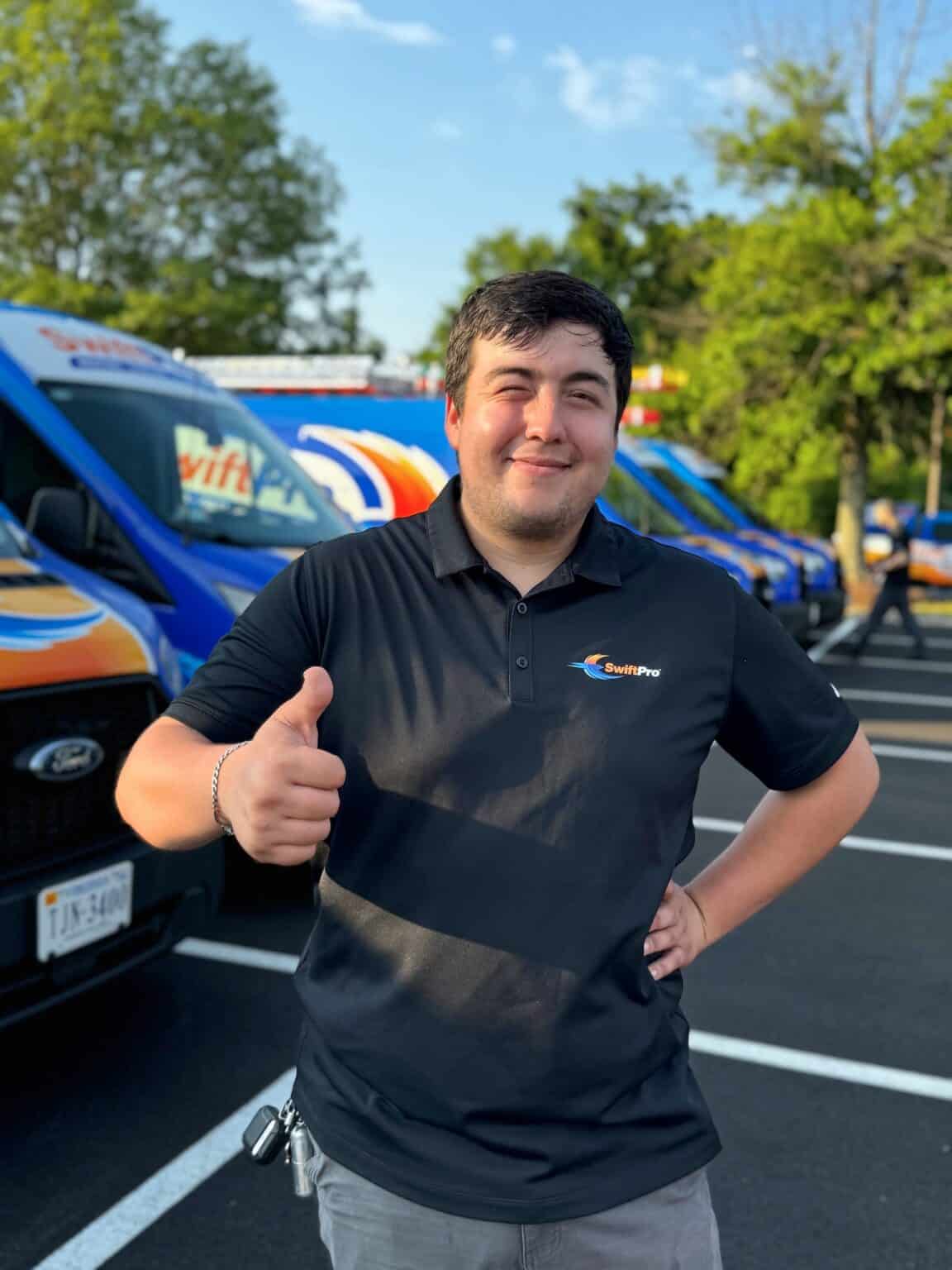 A smiling SwiftPro technician giving a thumbs up in front of the wrapped SwiftPro service vans at the company lot in Northern Virginia