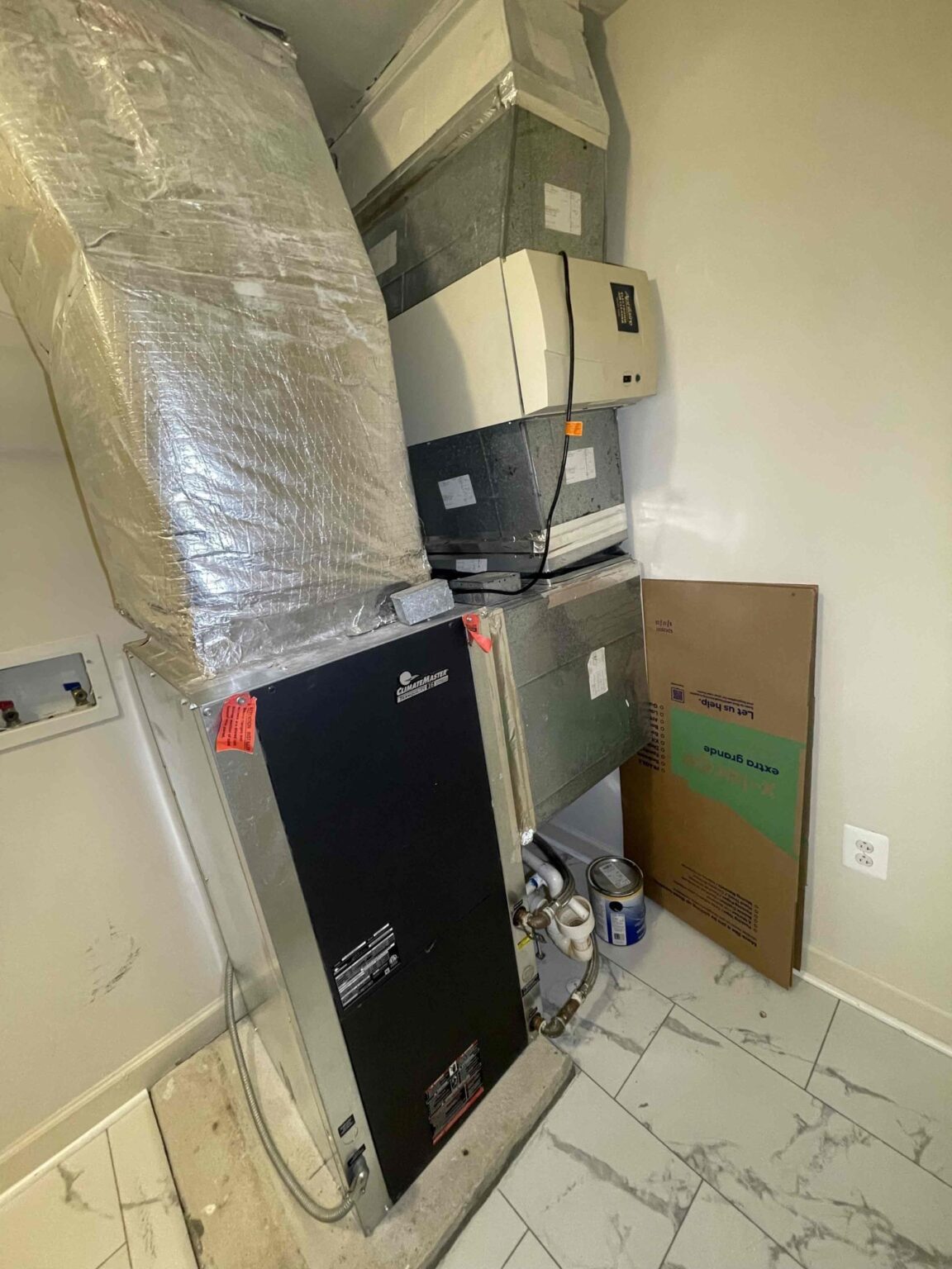 A whole house humidifier mounted on the ductwork above a heat pump unit in a Northern Virginia utility closet, foil insulated duct beside it