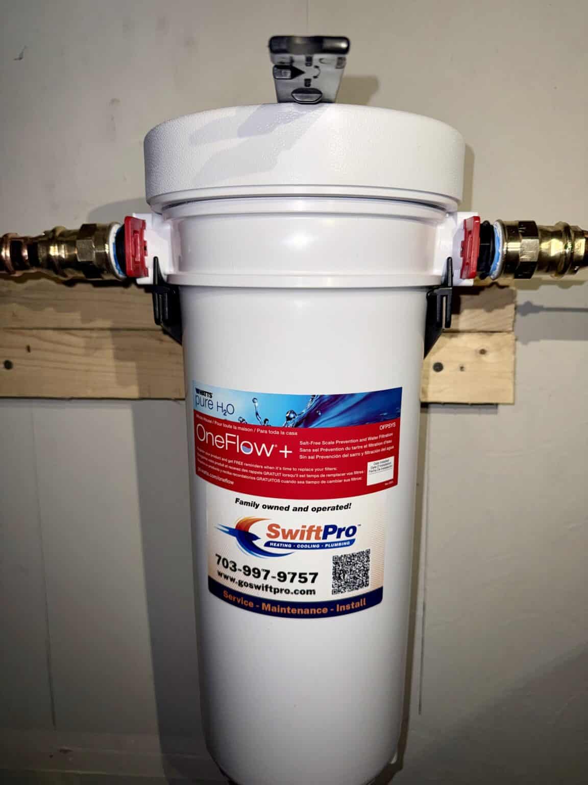 A white scale prevention water filter with a SwiftPro sticker, installed on brass fittings on a basement water line in Northern Virginia