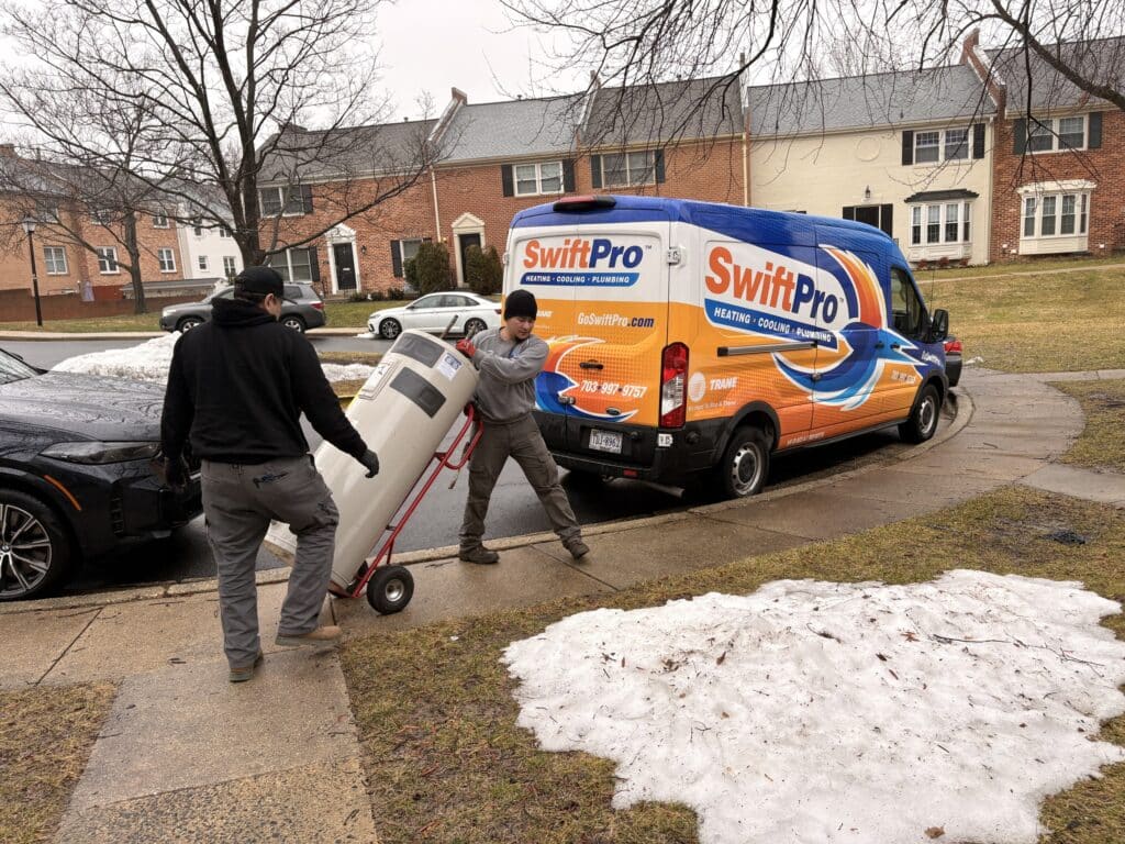 Two SwiftPro technicians wheeling a new water heater on a hand truck from a wrapped SwiftPro van to a Northern Virginia home