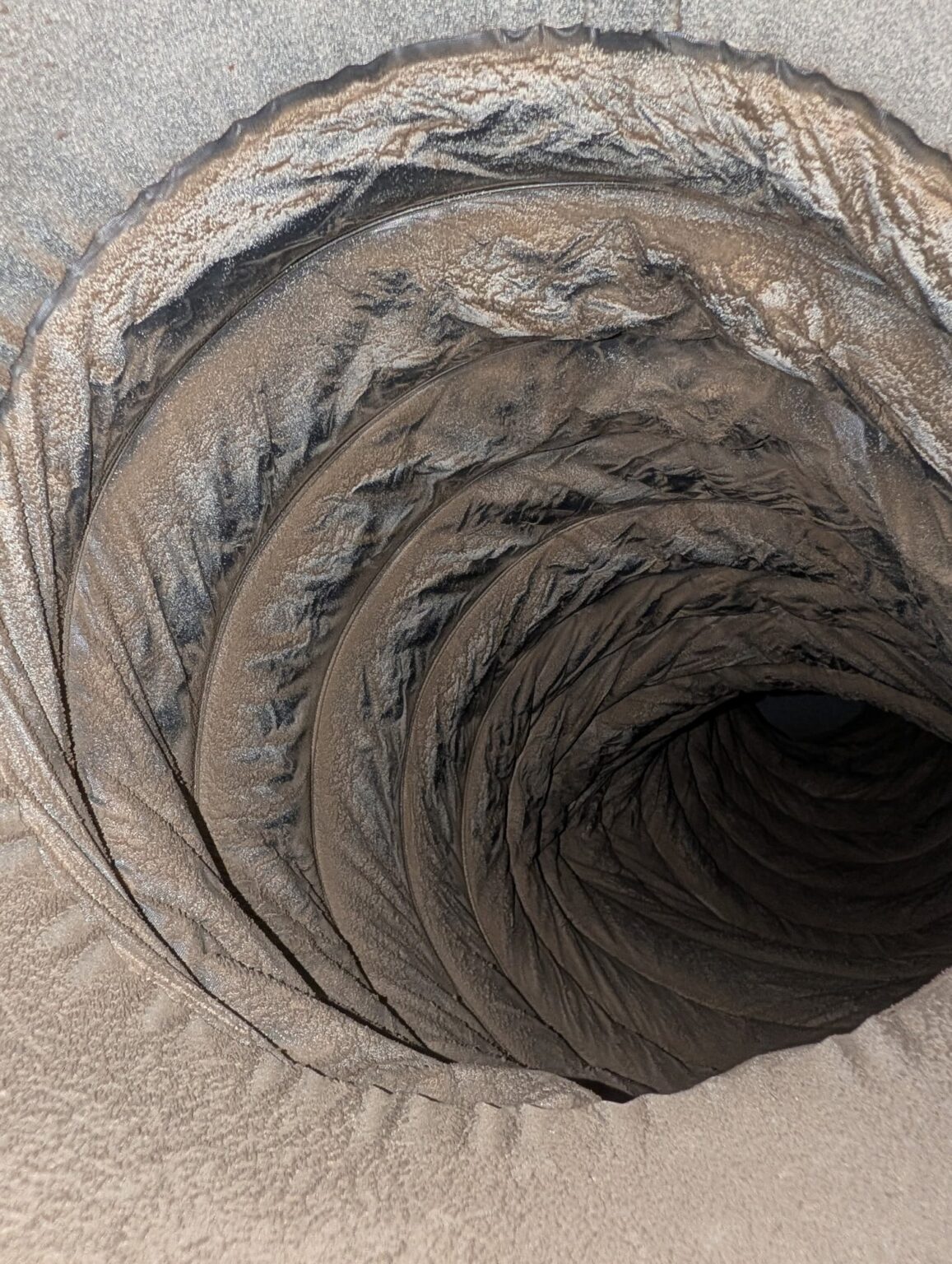 The inside of a flexible duct in a Northern Virginia home packed with a thick grey layer of dust and lint before cleaning