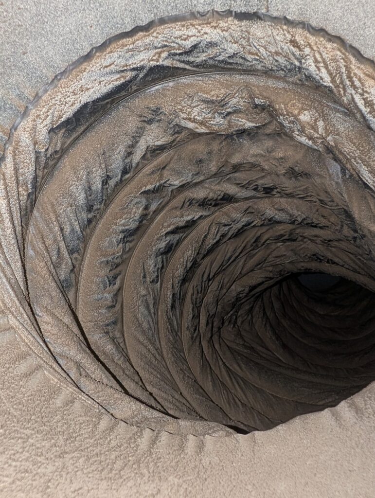 Looking down a flexible duct in a Northern Virginia home with grey dust and lint packed into every corrugation, before SwiftPro cleaned it