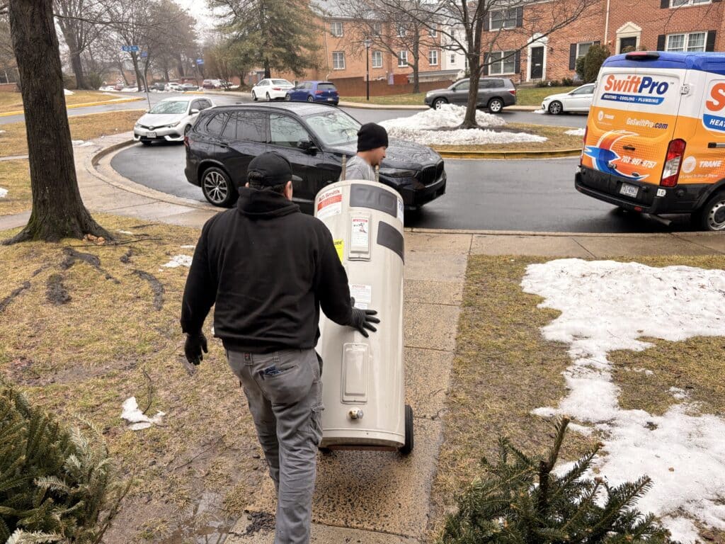 A SwiftPro technician carrying a new water heater across a driveway to a Northern Virginia home.