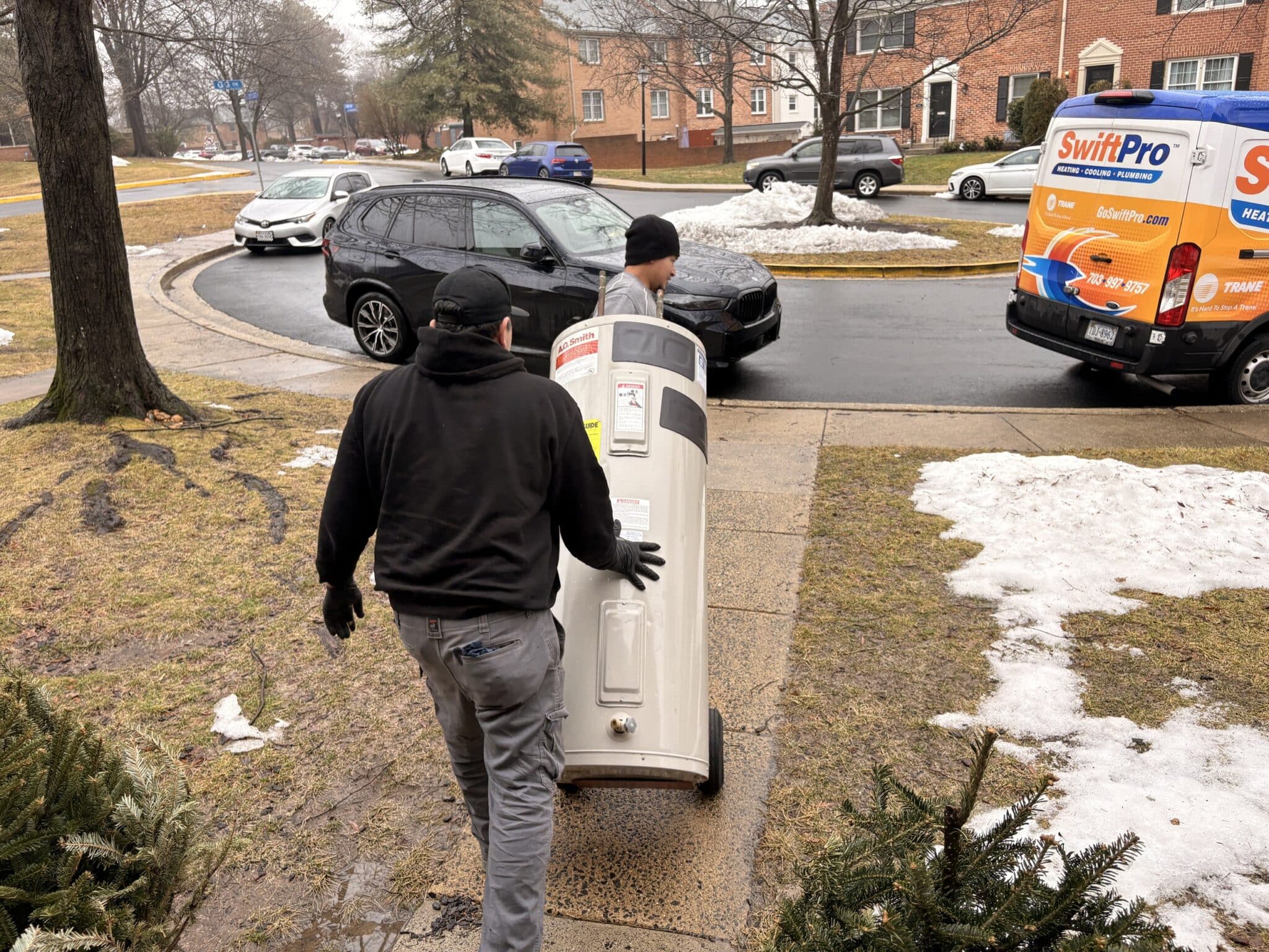 SwiftPro plumbers carrying a new A.O. Smith water heater in from the van on a winter morning in Northern Virginia