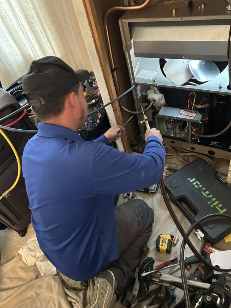 A SwiftPro technician taking readings inside the open electrical panel of an outdoor unit