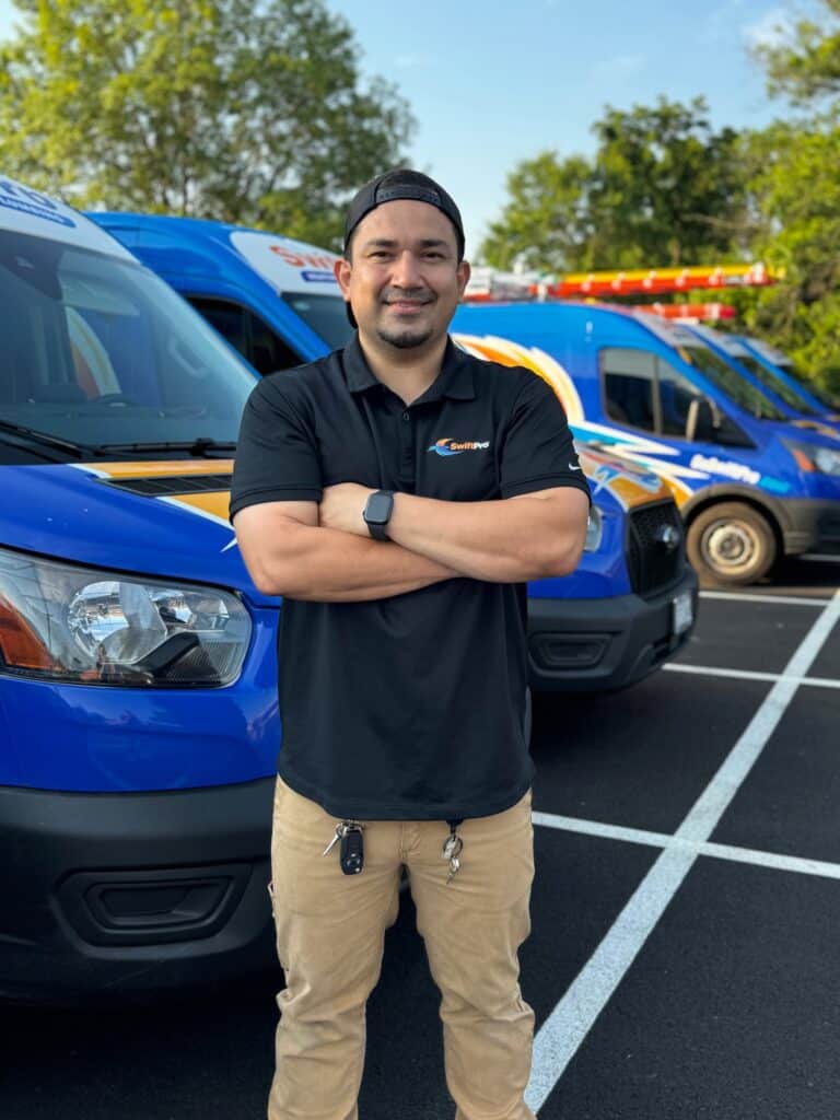 A SwiftPro technician standing with arms crossed in front of the wrapped SwiftPro van fleet