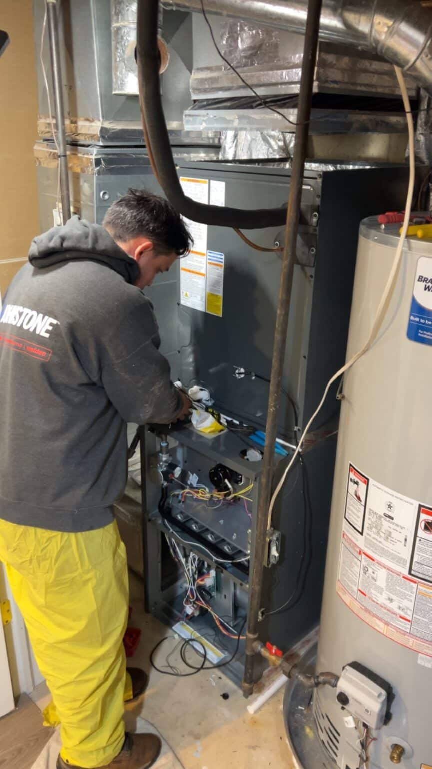 A SwiftPro technician working on the gas control valve of a tank water heater in a Northern Virginia home