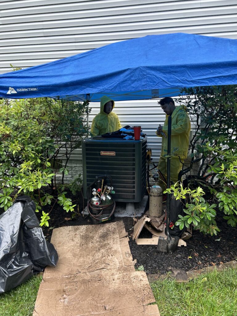Two SwiftPro technicians working on an outdoor unit under a pop-up canopy in wet weather in Northern Virginia