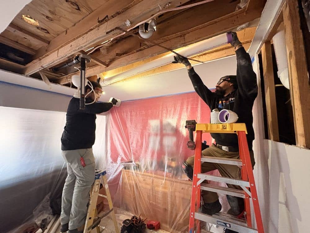 Two SwiftPro technicians working overhead on ceiling ductwork behind protective sheeting inside a Northern Virginia home