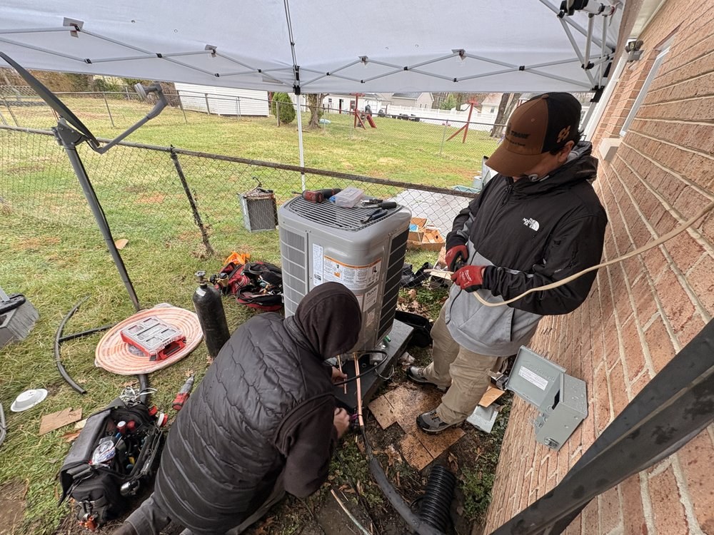 Two SwiftPro technicians working on an outdoor heat pump under a pop-up canopy in wet weather at a Northern Virginia home