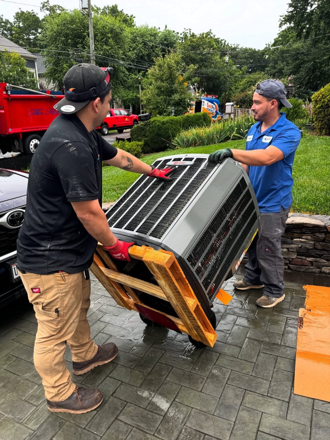 Two SwiftPro technicians moving a condensing unit on a dolly at a Northern Virginia home
