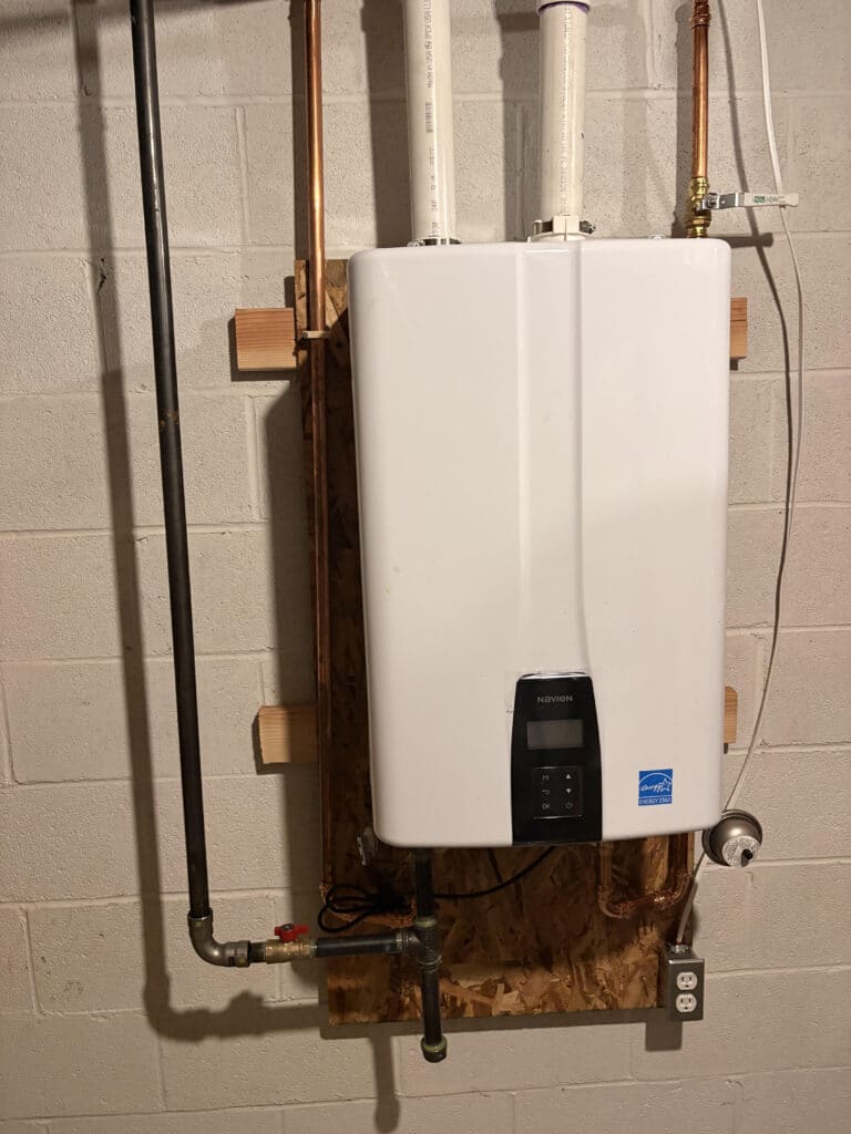 Tankless water heater mounted on a wooden panel in a basement setting.