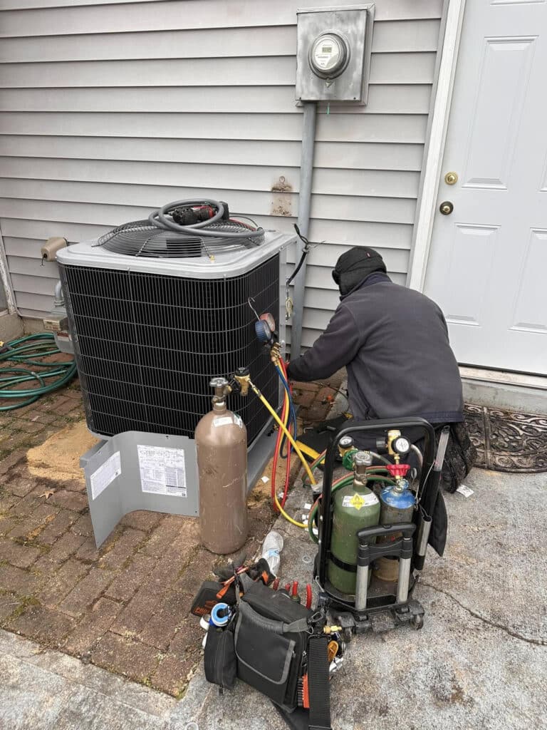 Technician servicing an outdoor air conditioning unit with tools and equipment.