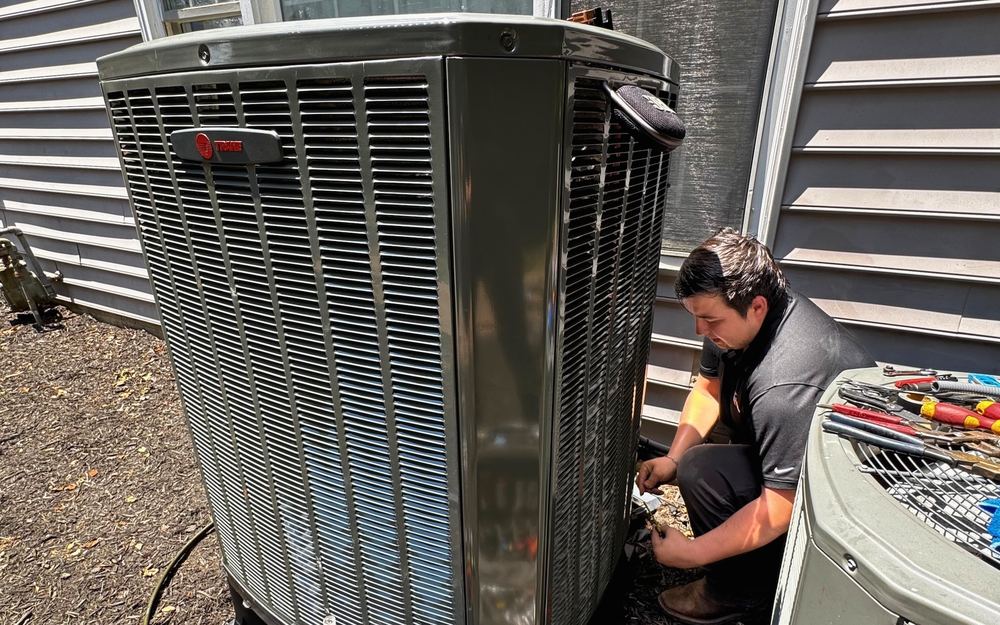 A SwiftPro technician kneeling beside a Trane outdoor AC unit at a Northern Virginia home, tools laid out on the unit next to it