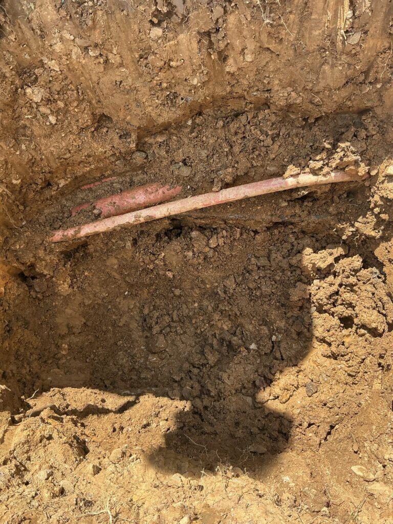 A trench SwiftPro dug in a Northern Virginia yard, exposing the buried copper water service line that feeds the house