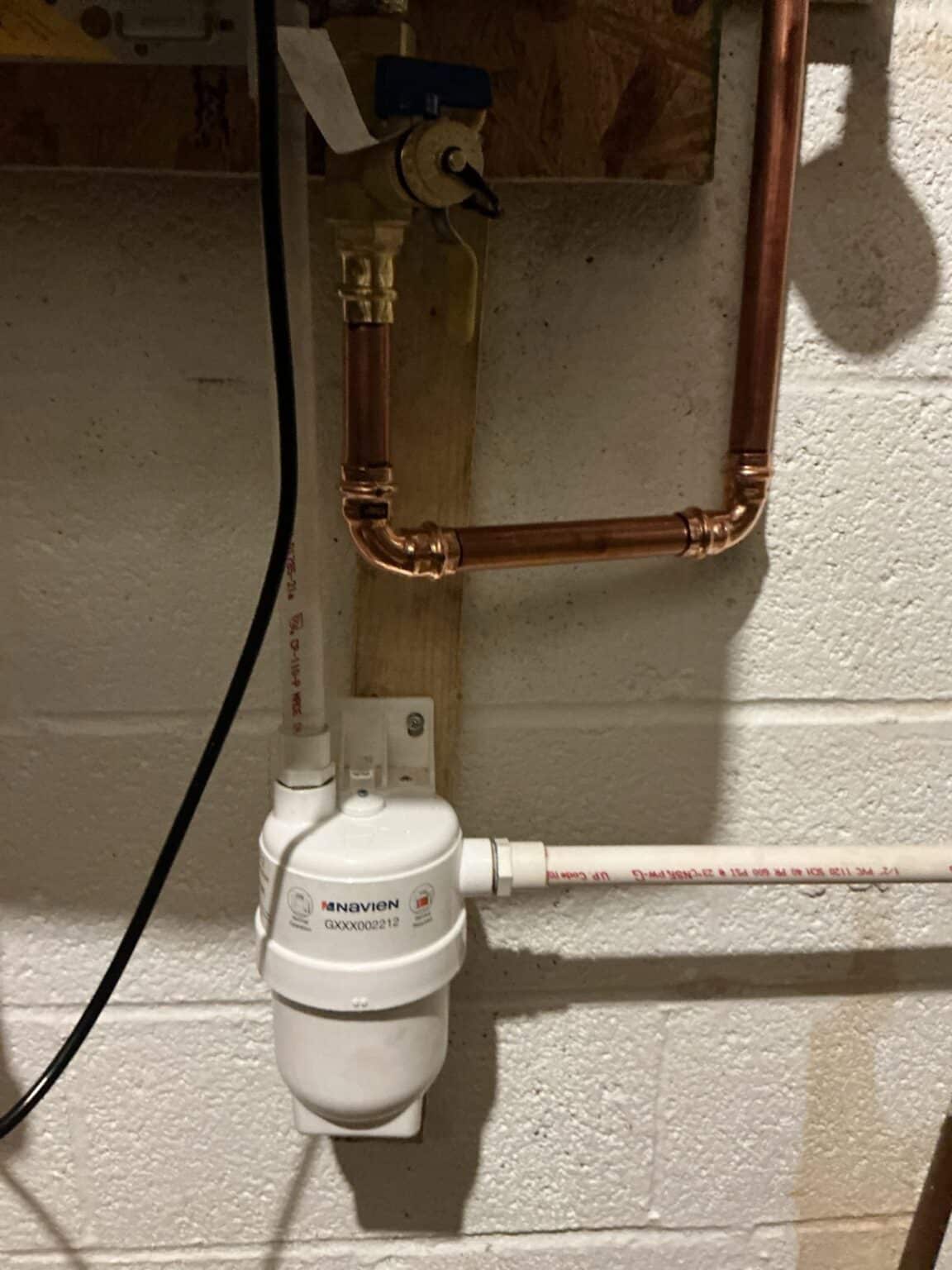 A white condensate neutralizer under a tankless water heater, plumbed into the drain line on a block basement wall in Northern Virginia