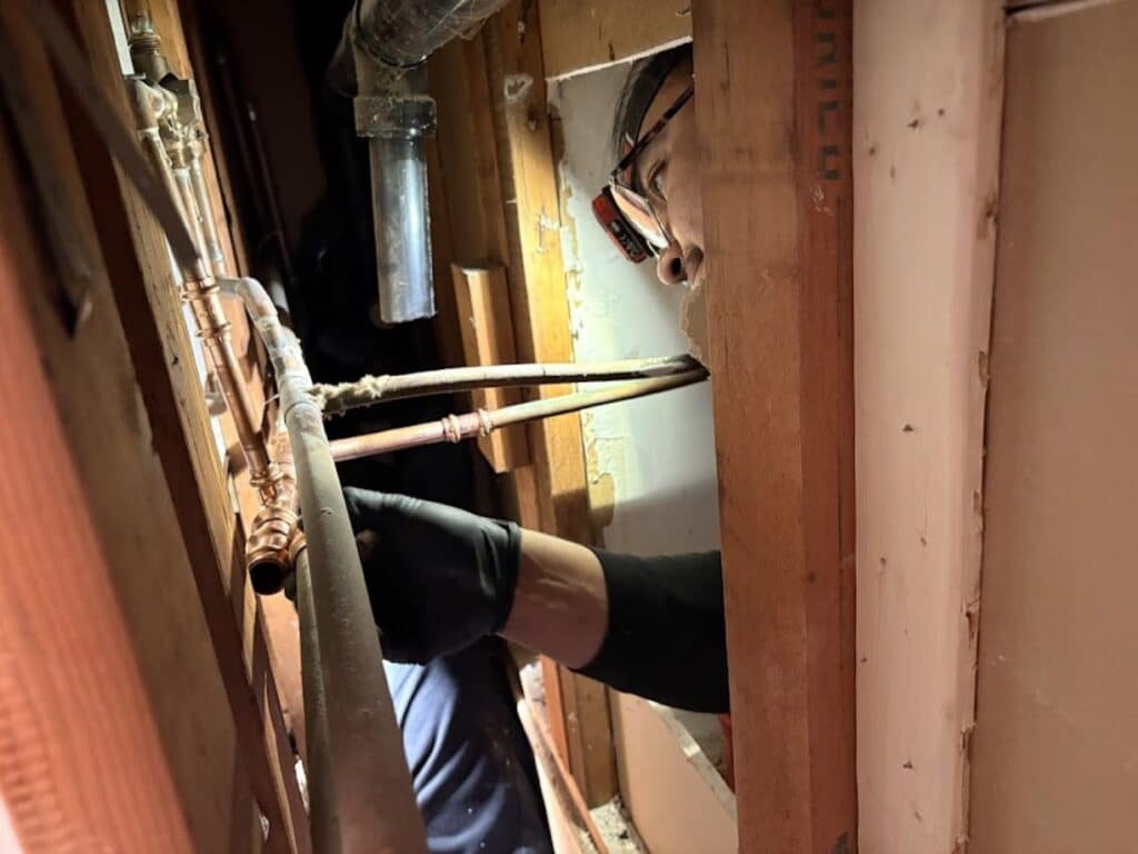 A SwiftPro plumber working on copper water supply lines inside an opened wall in a Northern Virginia home