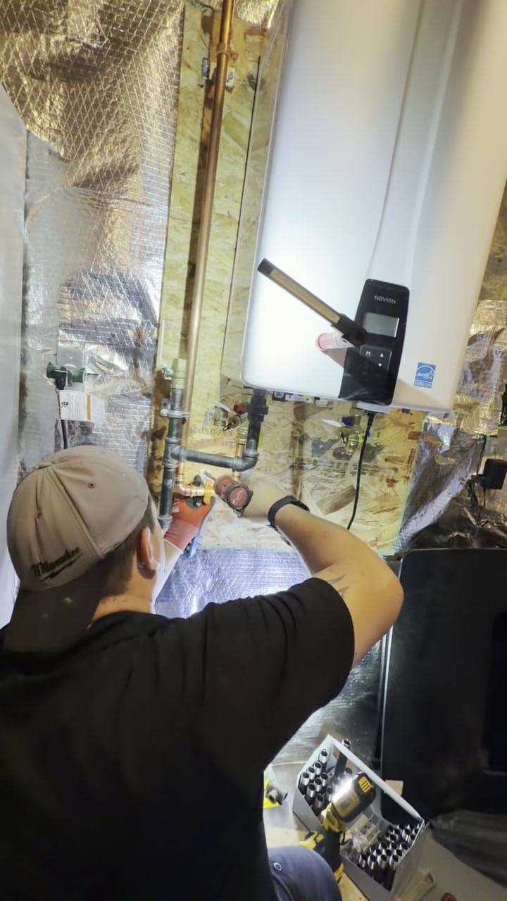 A SwiftPro plumber connecting the water and gas lines under a new Navien tankless water heater