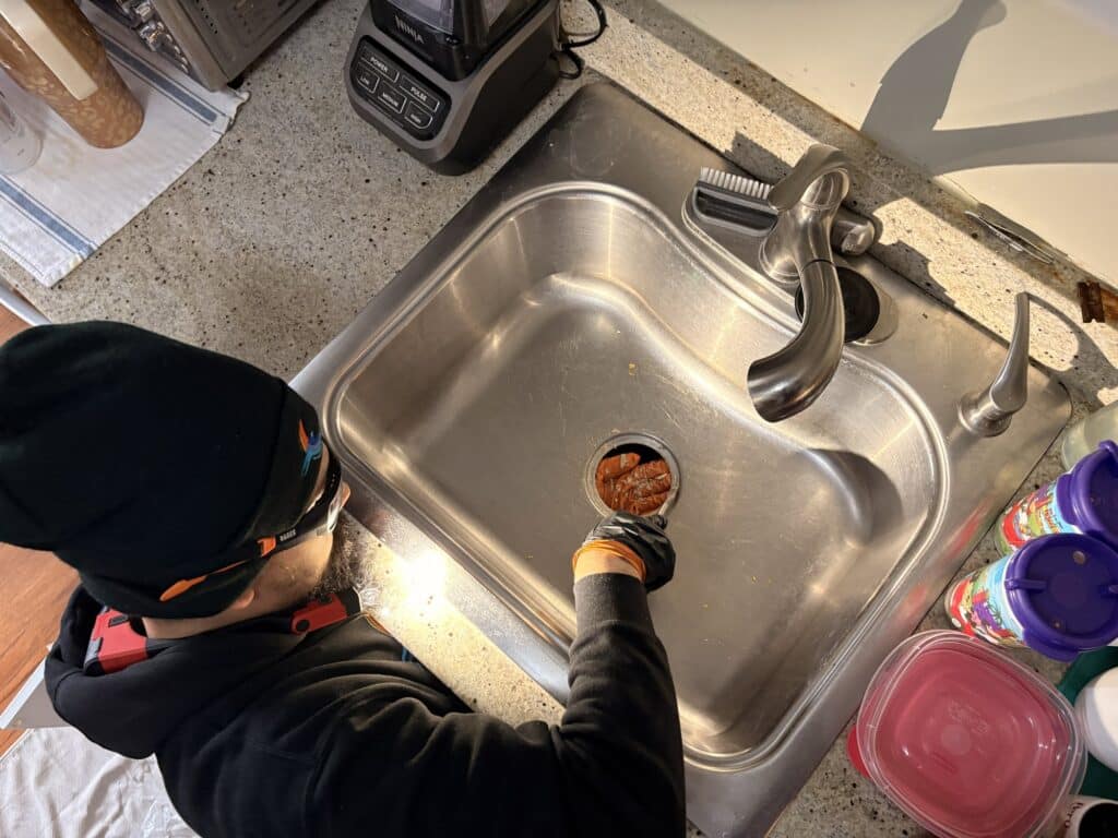 A SwiftPro plumber working under and at a stainless kitchen sink while clearing a blocked drain line in a Northern Virginia home