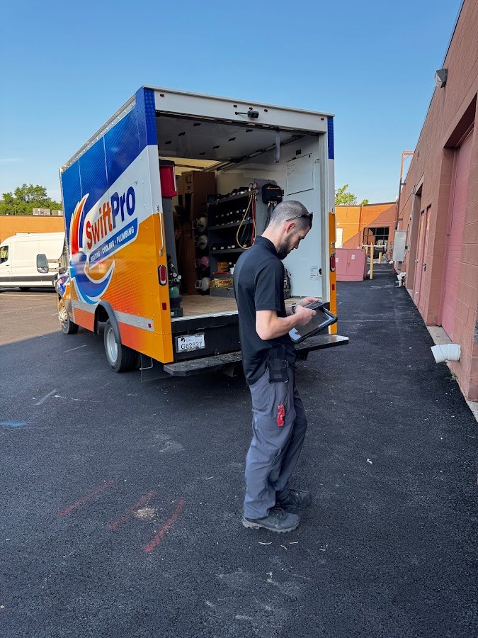 A SwiftPro technician standing at the open back of a wrapped SwiftPro van writing up a job on a tablet