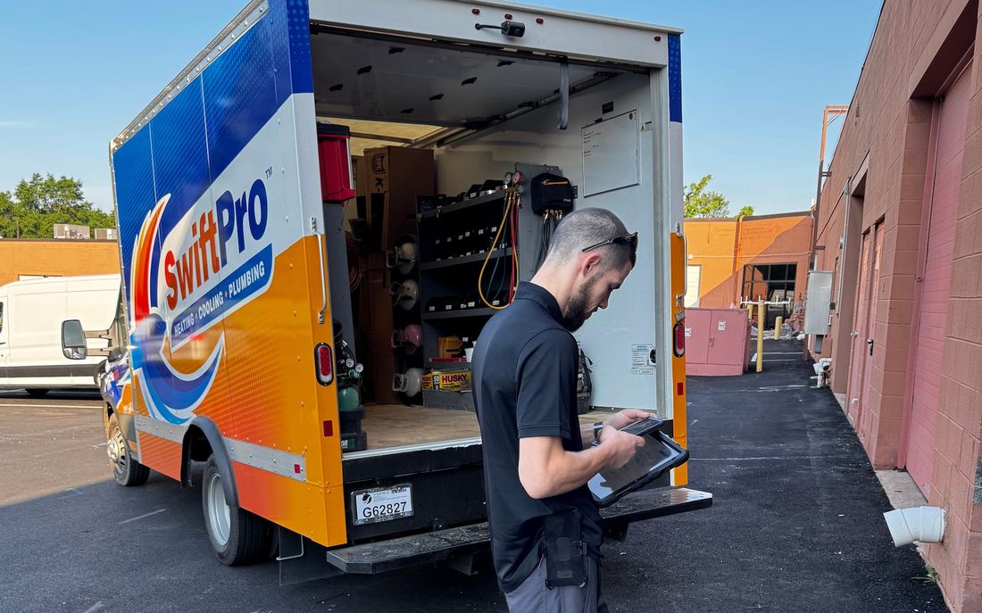 A SwiftPro technician at the back of a wrapped SwiftPro van in Northern Virginia, going over a visit's written report on a tablet
