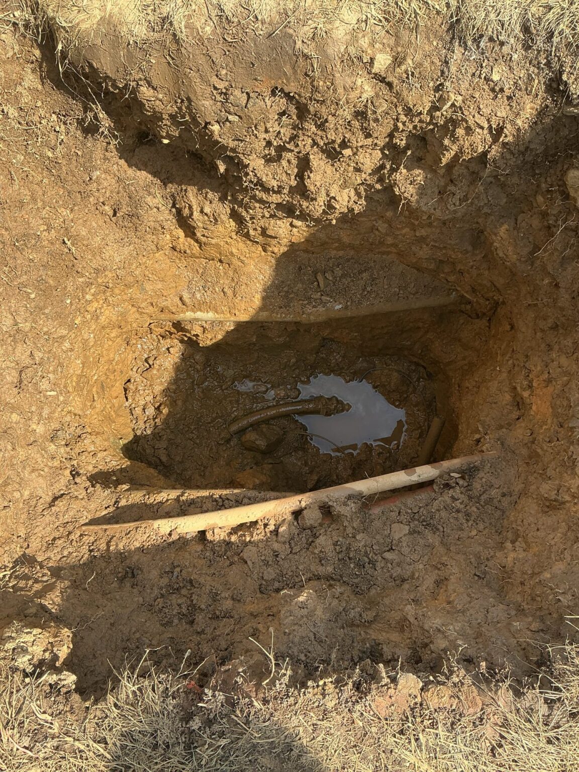 A dug trench in a Northern Virginia yard with water pooling around the failed underground pipe SwiftPro is replacing