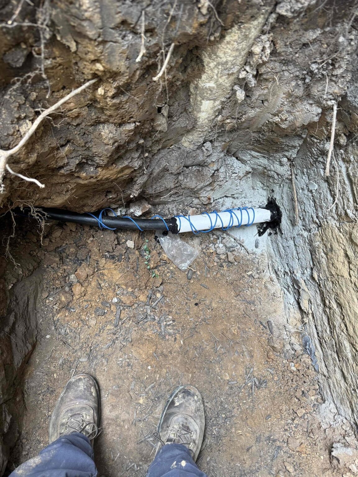 A SwiftPro technician standing over an excavated underground plumbing line surrounded by the rock and clay common in Northern Virginia soil