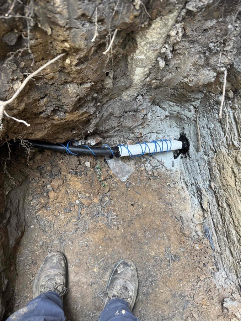A SwiftPro technician standing over an excavated underground plumbing line surrounded by the rock and clay common in Northern Virginia soil