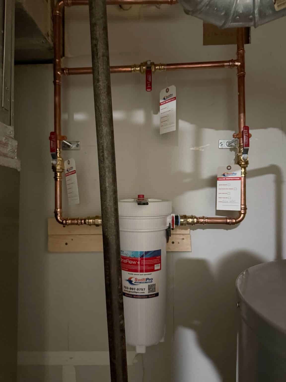 A whole house water filter installed by SwiftPro on a copper bypass loop with red handled shutoff valves, in a Northern Virginia utility room