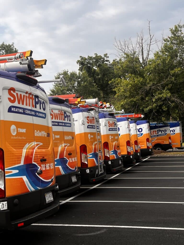 A row of wrapped SwiftPro Heating, Cooling and Plumbing service vans parked side by side with ladders on the roof racks