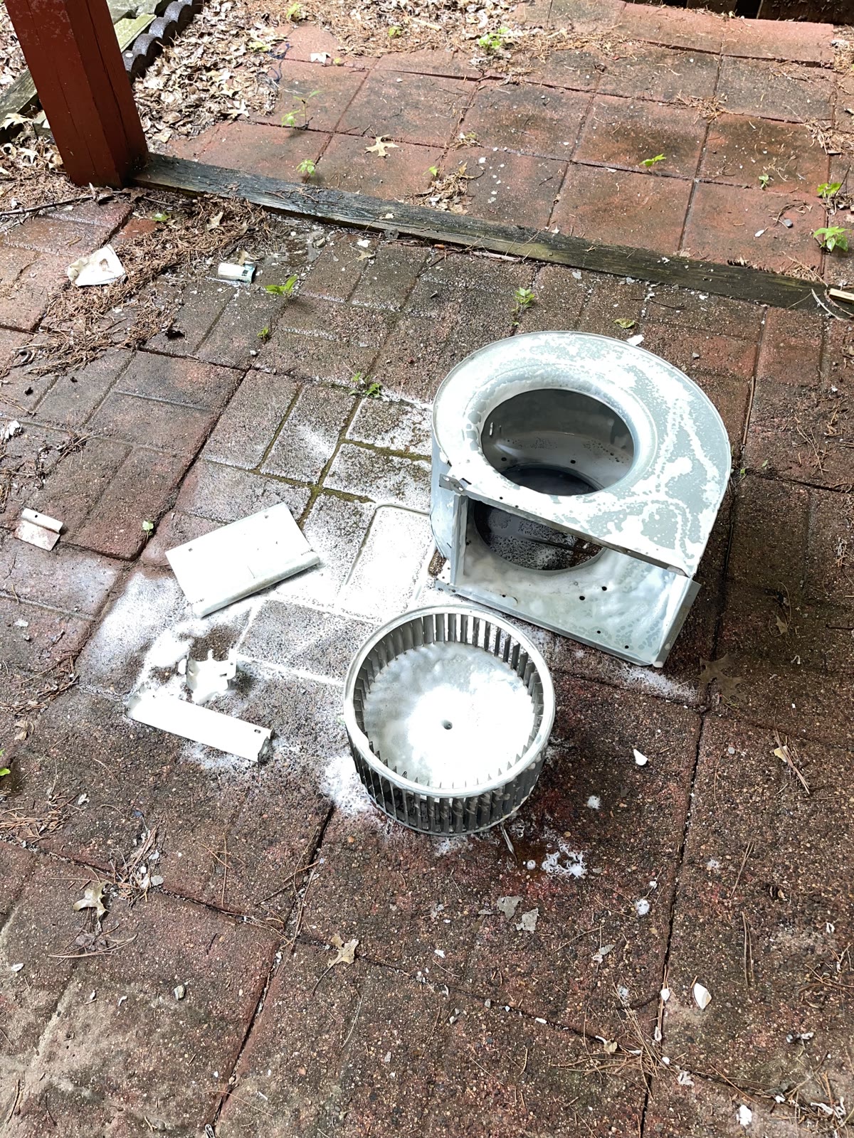 Blower wheel and metal housing separated on a patio with cleaning foam on the components.