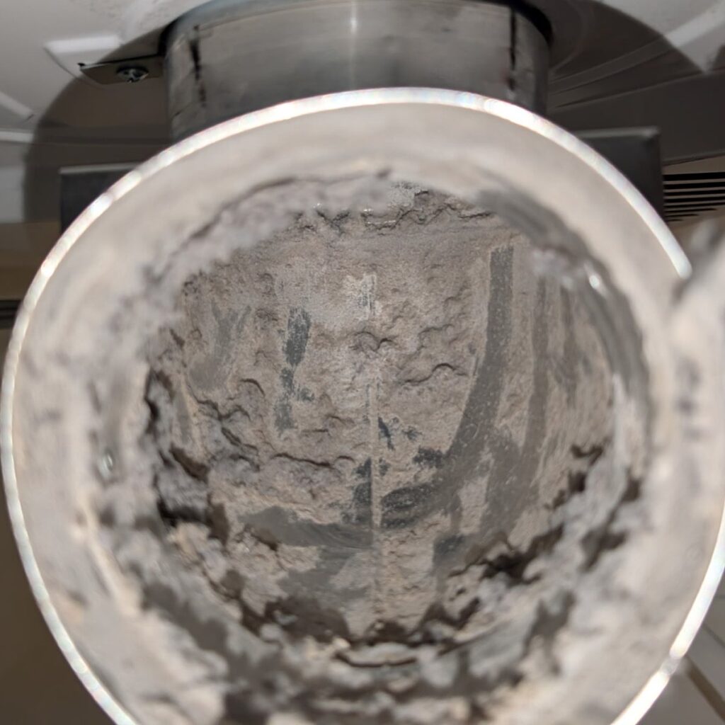Inside a metal dryer vent pipe before cleaning, its walls caked with grey lint and the opening narrowed, on a SwiftPro dryer vent cleaning in Northern Virginia