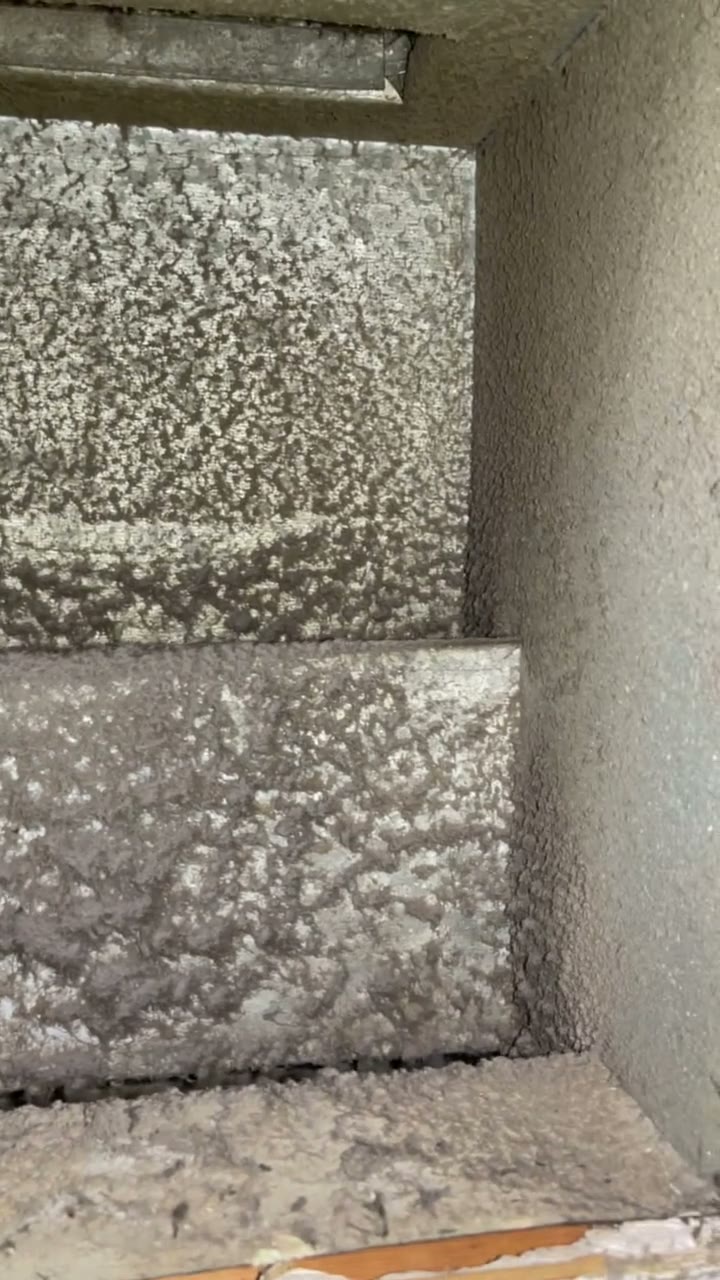 Raw phone clip, no text: heavy grey dust caked on every wall of a duct plenum before cleaning.