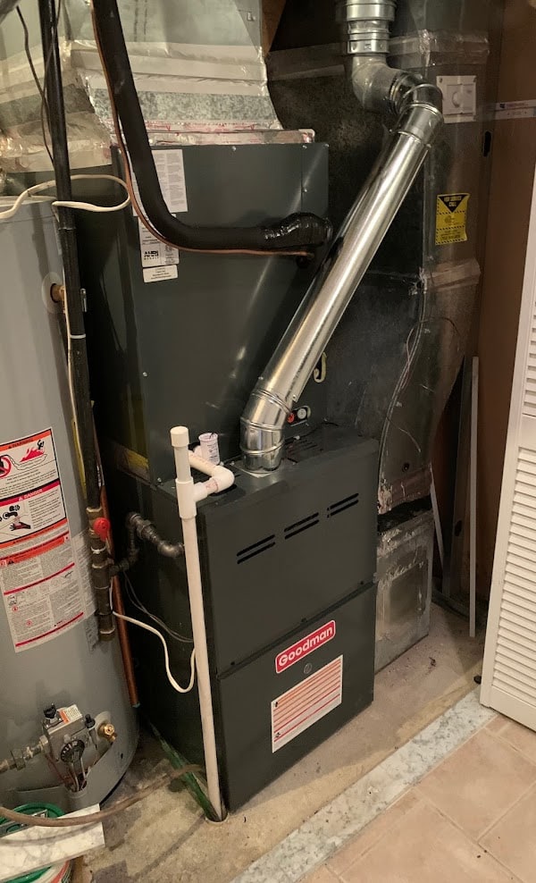 A gas furnace with the evaporator coil cabinet on top, a black insulated refrigerant line into the coil and a white condensate drain pipe running to the floor, Northern Virginia
