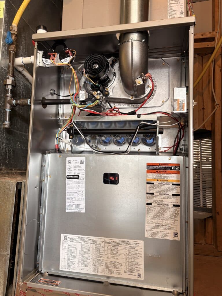 A gas furnace with its front panel off and the burners lit on a SwiftPro job in an Ashburn, Virginia basement, the inducer fan and flue pipe above the burners