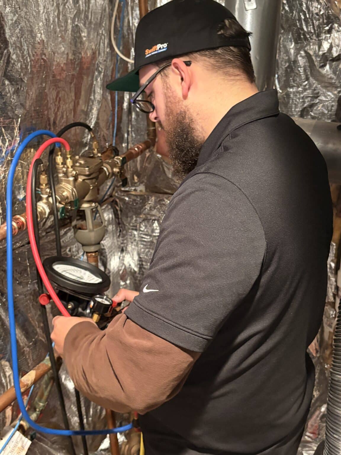 A SwiftPro plumber testing an RPZ backflow preventer with a gauge kit in an Ashburn, Virginia basement