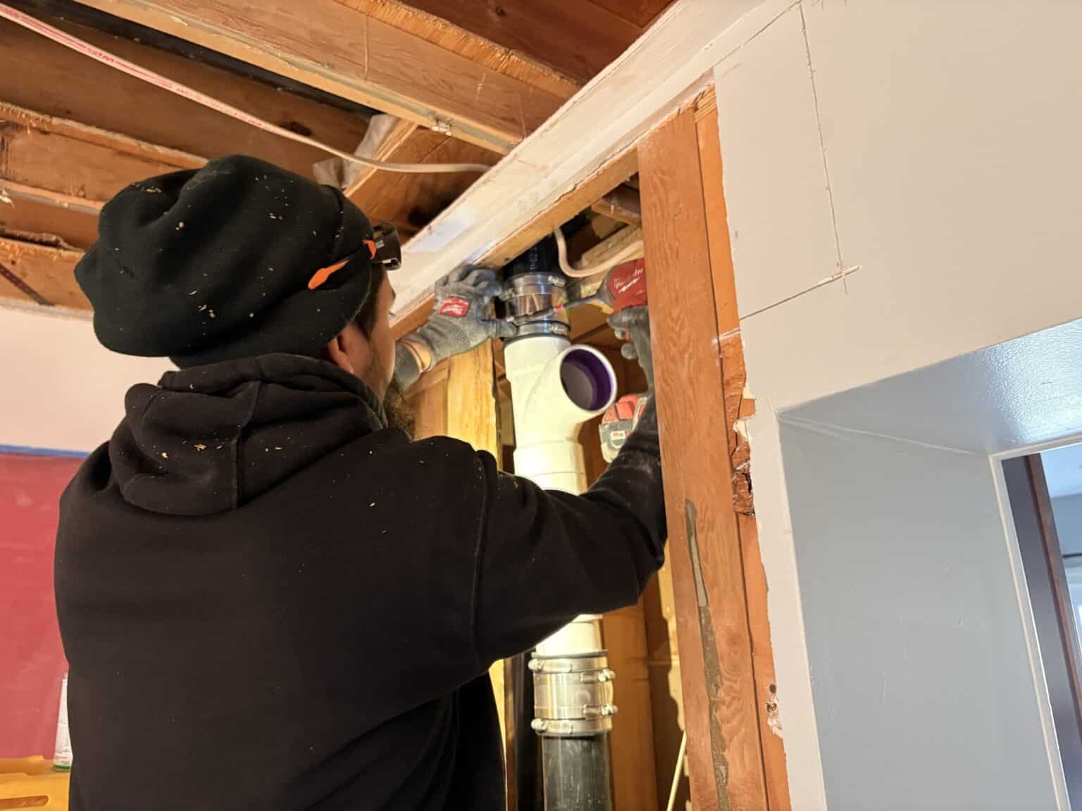 A SwiftPro plumber joining new PVC drain pipe to a home's drain stack inside an opened wall in Northern Virginia