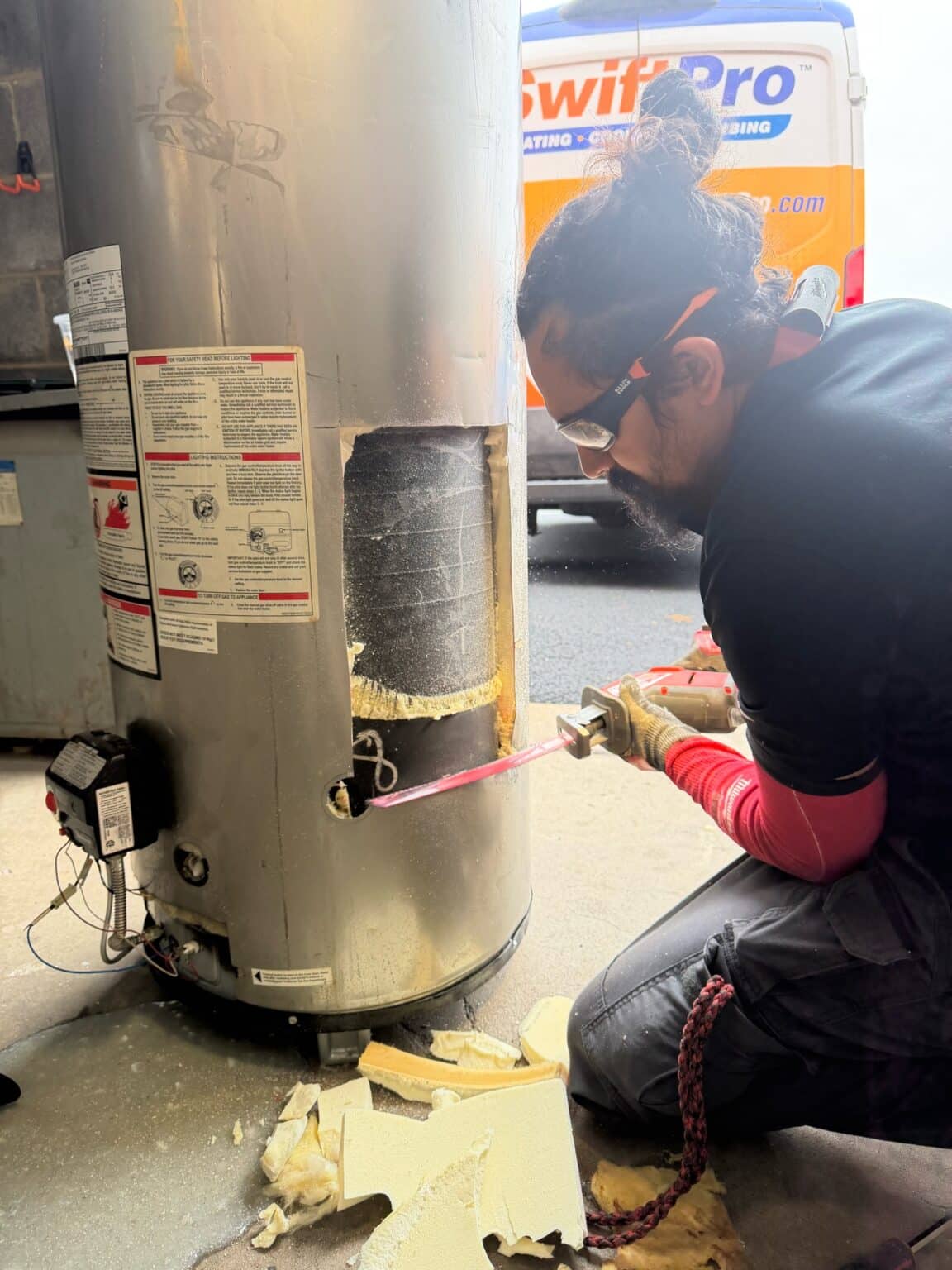A SwiftPro plumber cutting open an old gas water heater in the bay at SwiftPro's Chantilly, Virginia shop, showing the steel tank and foam insulation