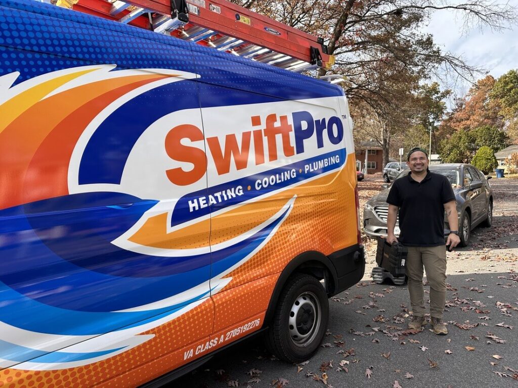 A smiling SwiftPro technician beside a wrapped SwiftPro van parked on a Northern Virginia street in the fall, the Virginia Class A license on the van's back corner