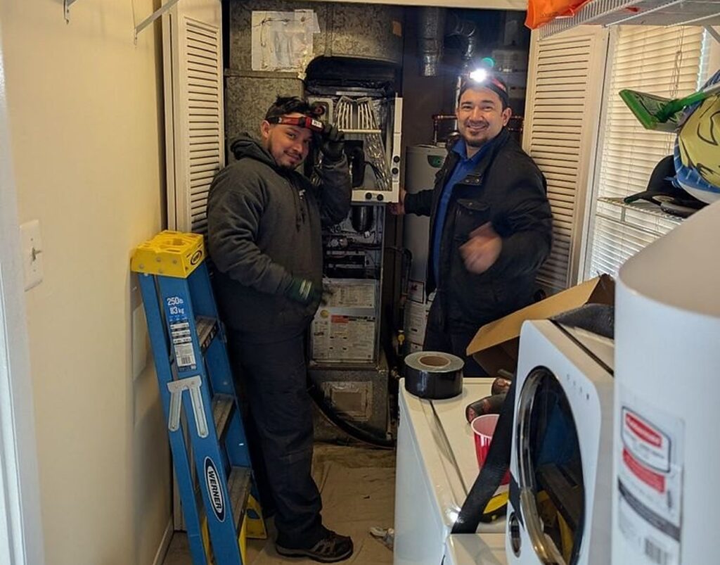 Two SwiftPro technicians in a Northern Virginia utility room, at the open furnace with the tank water heater behind them