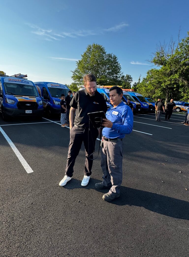 Two SwiftPro technicians going over a work order on a tablet in front of the van fleet in Northern Virginia