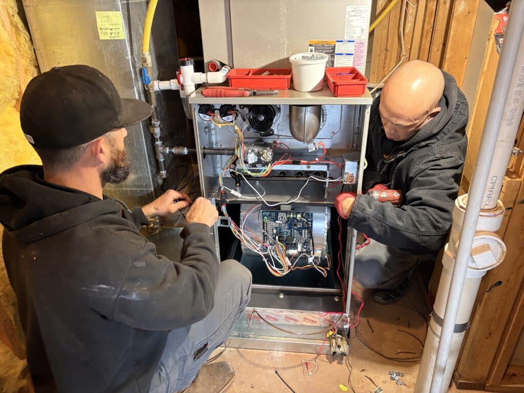 Two SwiftPro technicians wiring a new Carrier gas furnace in an Ashburn, Virginia basement