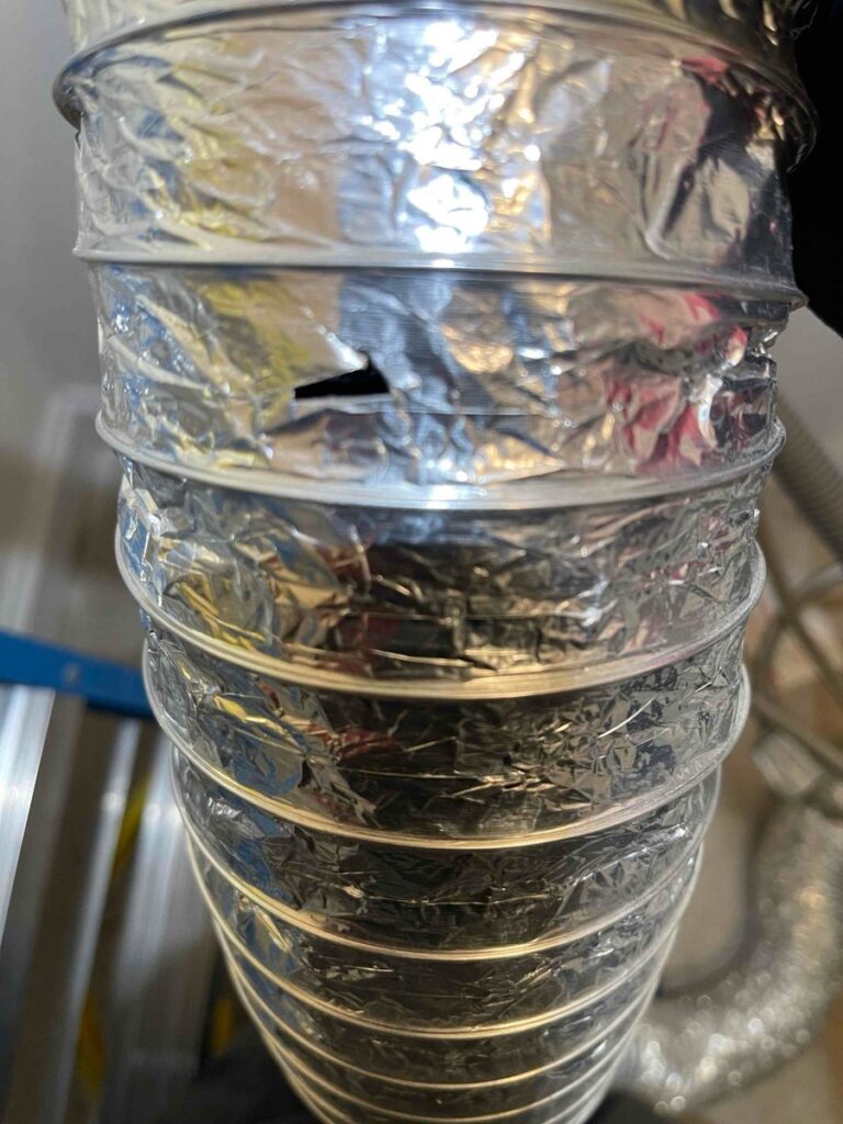 A crinkled foil dryer vent hose with a tear through the foil between two of its wire rings, found by a SwiftPro technician on a dryer vent cleaning in Northern Virginia