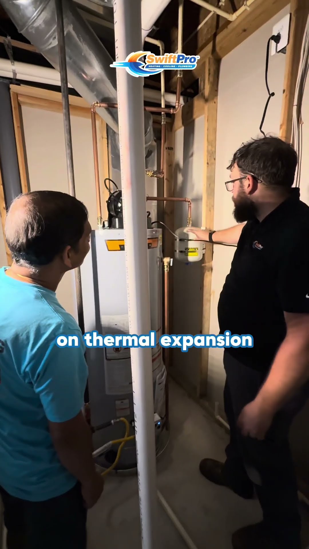 A tech walks a homeowner through a gas water heater install in an unfinished basement, pointing at the expansion tank area and piping while captions talk about thermal expansion.