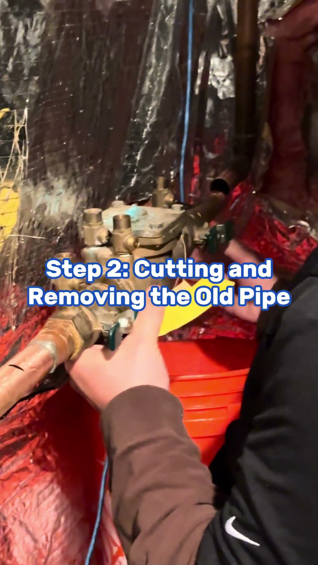 Step-by-step pipe replacement under a kitchen sink: a bearded tech in a black hoodie holds up a small clear part, a tech in a brown sleeve cuts out an old brass valve and pipe behind foil heat shieldi