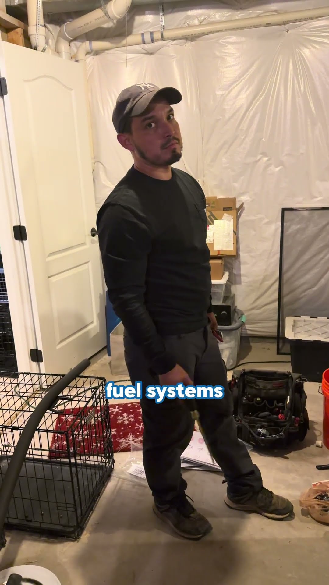 A tech squats at a furnace in an unfinished basement with a Milwaukee tool bag, then stands and talks to camera about dual-fuel systems (heat pump plus gas furnace).