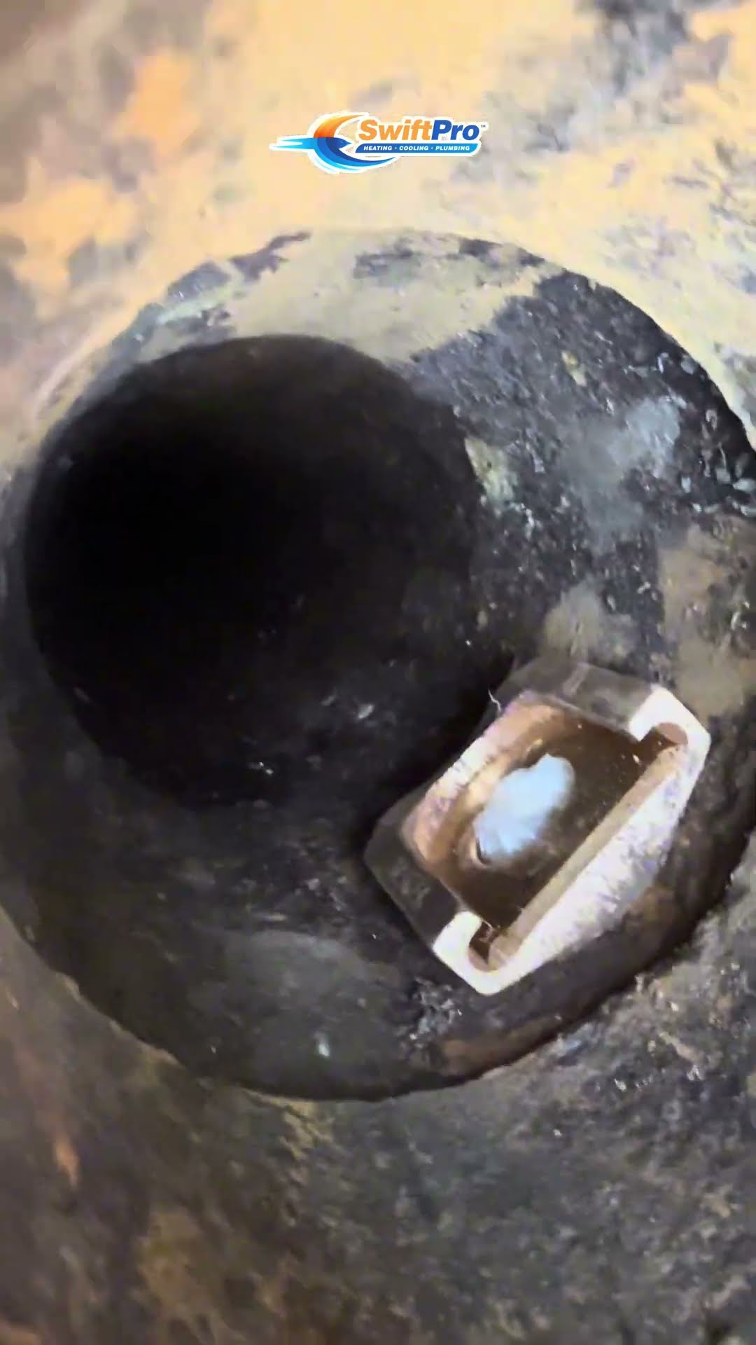 A tech kneels in a basement window well beside a brick house scooping gravel into red buckets, a close-up looking down into a round drain opening in the well, and buckets of gravel lined up outside.
