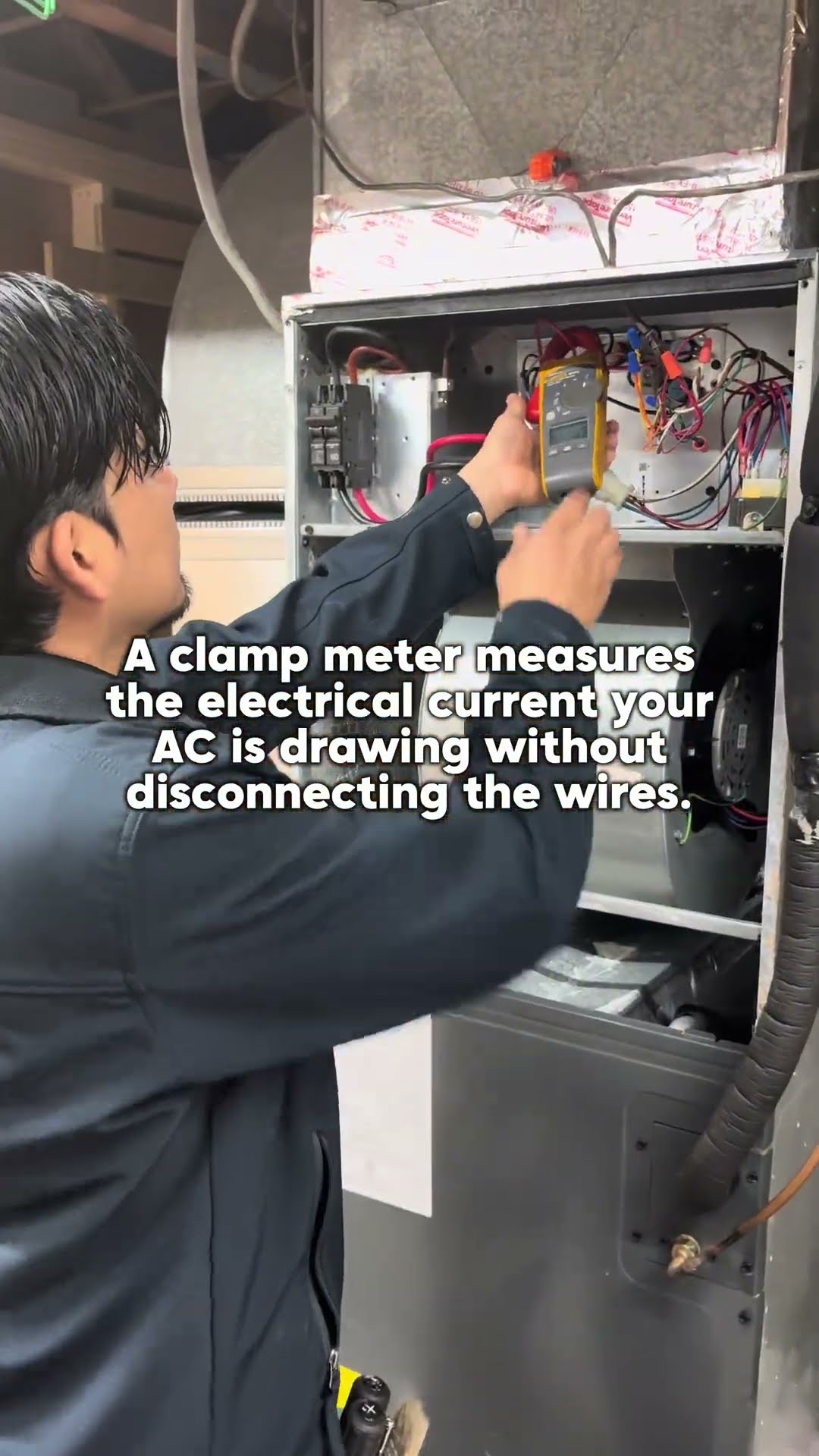 A tech uses a clamp meter on the wiring inside an air handler control panel, with on-screen text explaining it reads current without disconnecting wires.